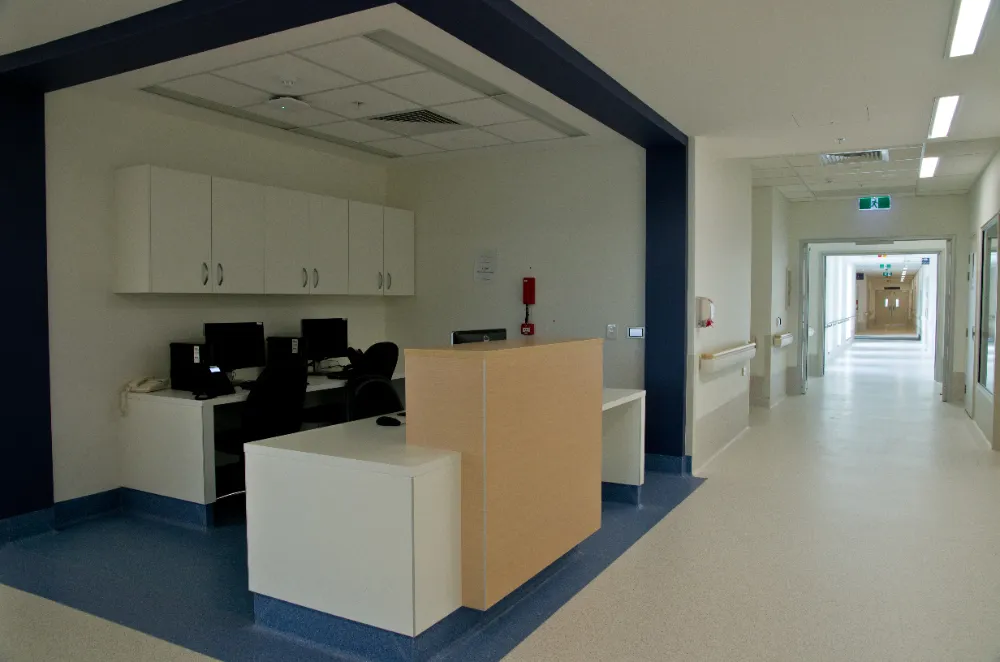 Poste de soins d'un hôpital avec comptoir blanc et bois clair, couloir en arrière-plan